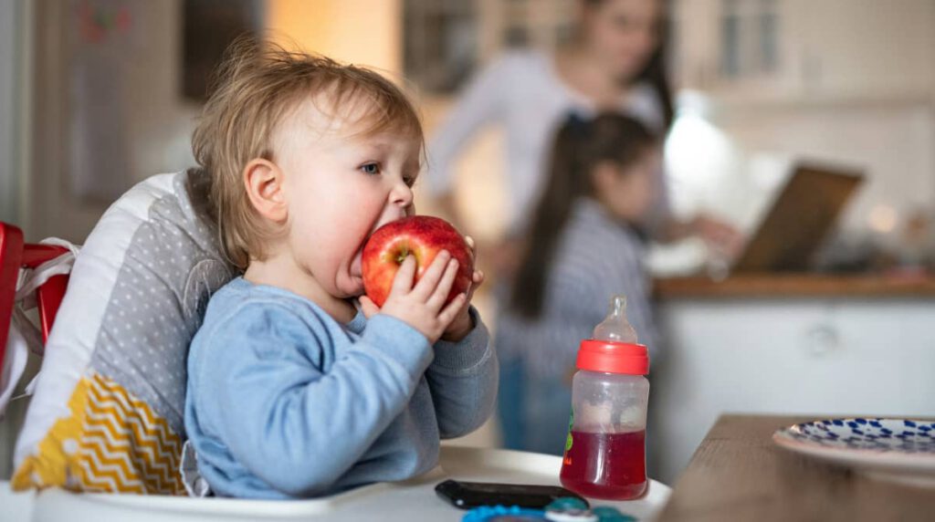 Un bebé muerde una manzana entera, mostrando sus dientes de leche y una expresión de felicidad. La imagen resalta la importancia de una buena salud dental y el desarrollo adecuado de los dientes en los niños.